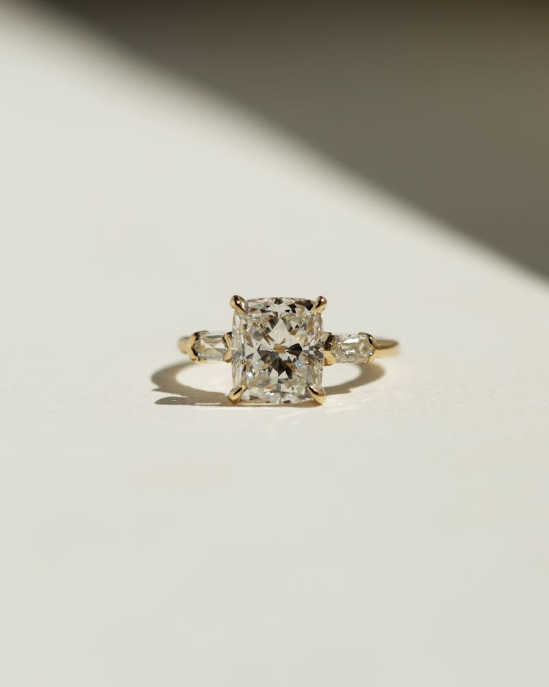 a prong-set radiant-cut diamond engagement ring with two side baguettes in yellow gold by Grace Lee