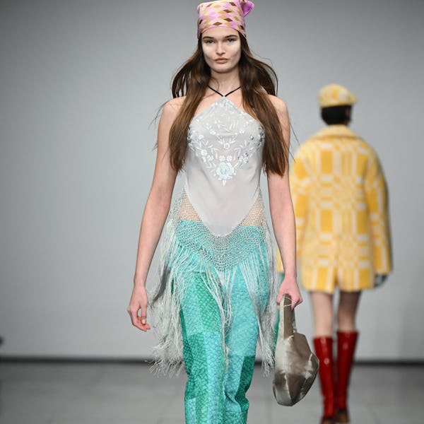 a model wearing a fringe halter top and low-rise turquoise pants on the Conner Ives runway