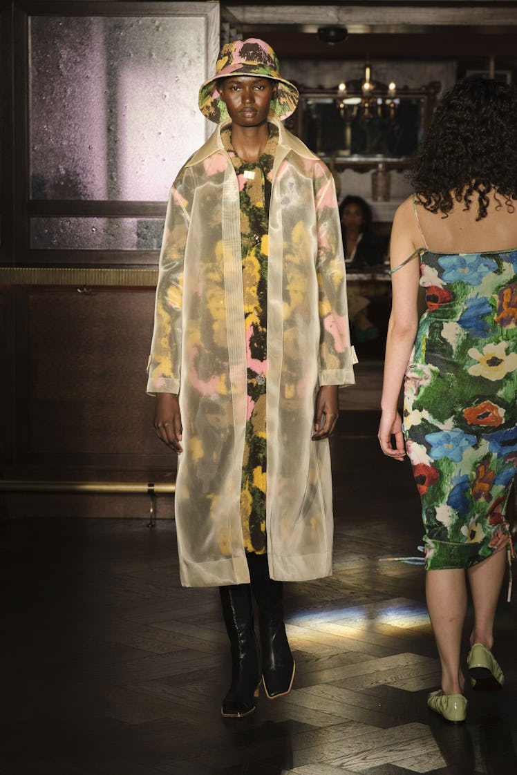 A model in a floral dress and a translucent raincoat and a bucket hat by Rejina Pyo at the London Fa...