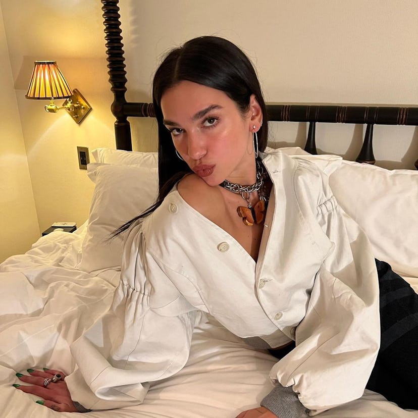 Dua Lipa with green nails posing on bed pucker