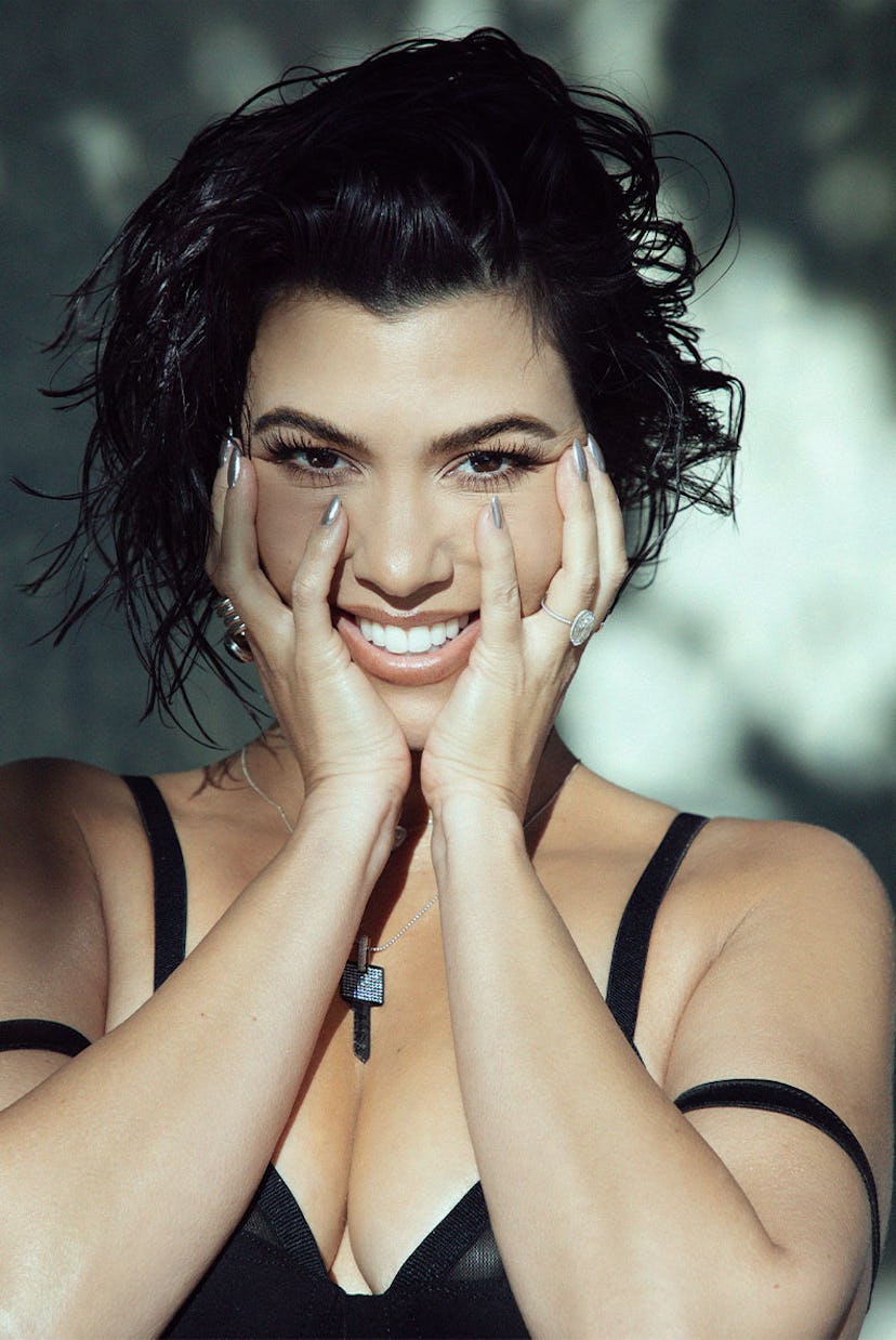 Kourtney in a Markoo bra top, EÉRA necklace, and Agmes earrings squishing her cheeks with her hands,…