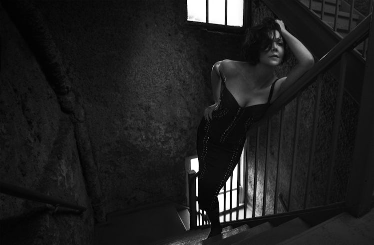 Maggie Gyllenhaal in a strappy dress posing on a staircase in black-and-white