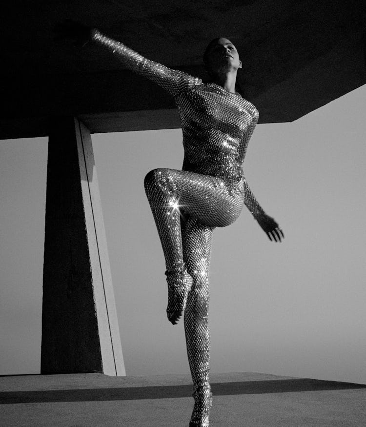 Zendaya in metallic body suit poses with one leg up. 