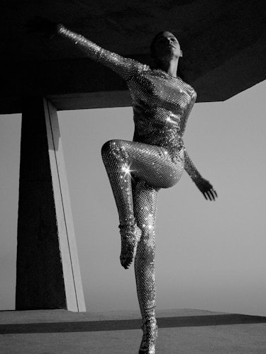 Zendaya in metallic body suit poses with one leg up. 