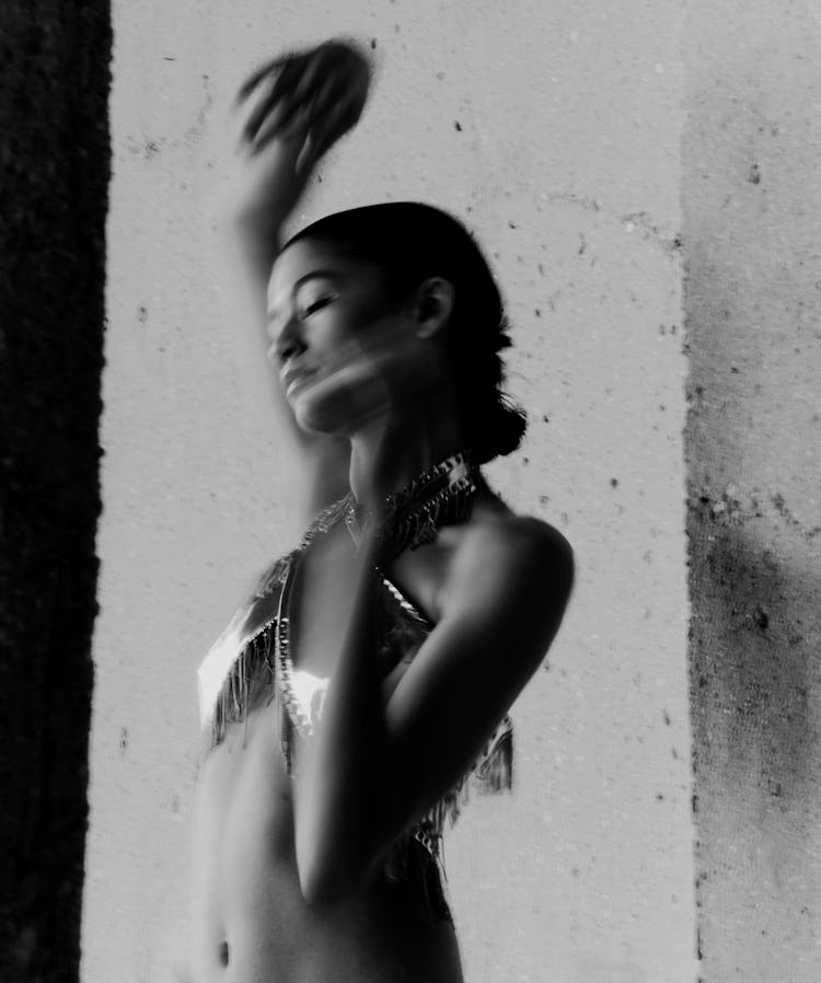 Zendaya in black and white portrait with arms raised.