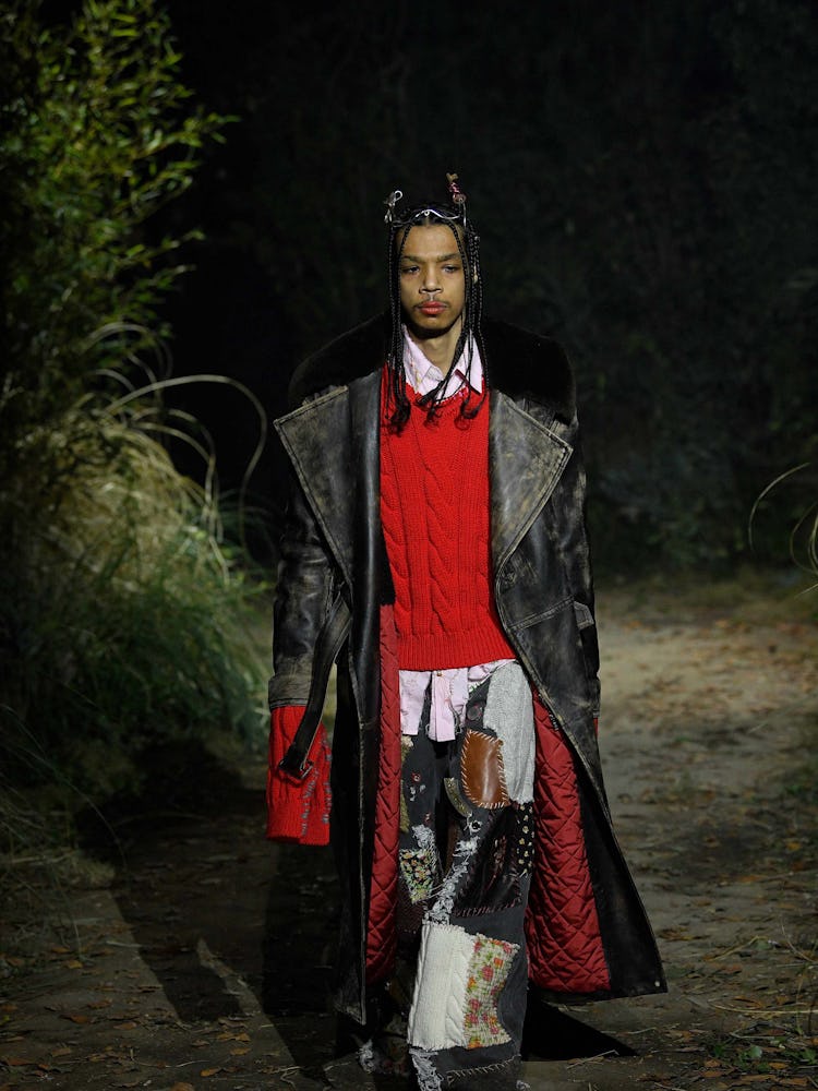 A model in a black leather long jacket, red sweater and patchy pants at walking the  Marni Fall 2022...