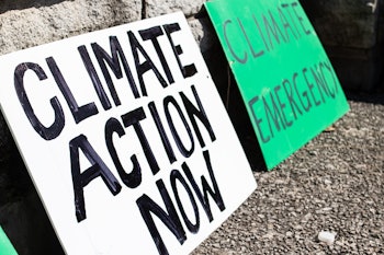 Two 'Climate action now' and 'climate emergency' signs rest on a sidewalk during a climate change ma...