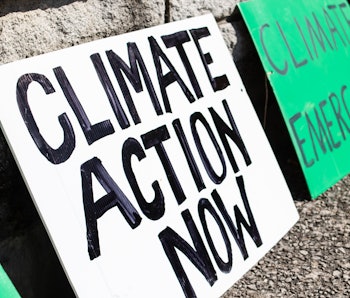Two 'Climate action now' and 'climate emergency' signs rest on a sidewalk during a climate change ma...
