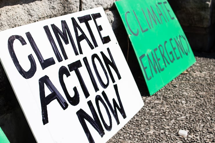Two 'Climate action now' and 'climate emergency' signs rest on a sidewalk during a climate change ma...