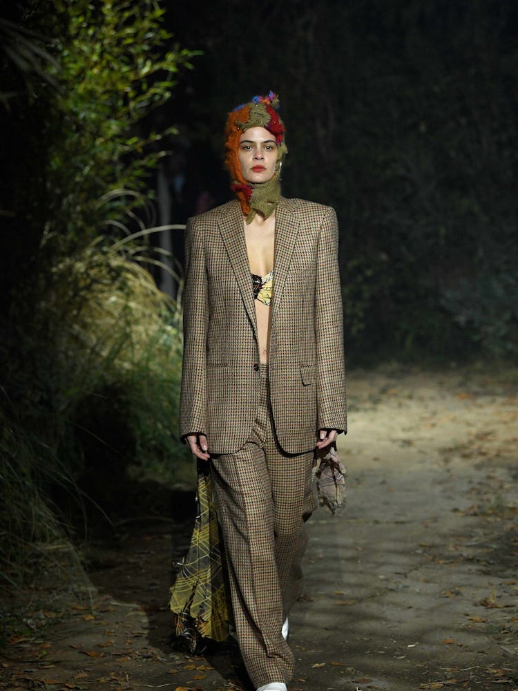 A model walking the runway in a beige checkered suit and bralette underneath 
