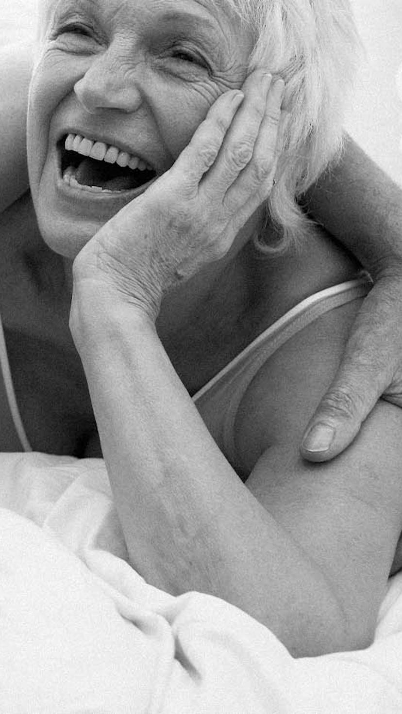 A long-term couple laughing while lying in a bed in their underwear