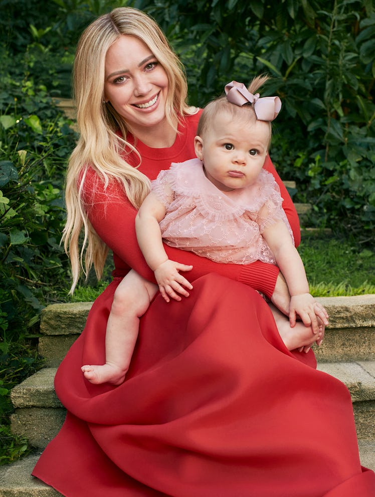 Hilary Duff posing for a photo while holding her daughter in her lap.
