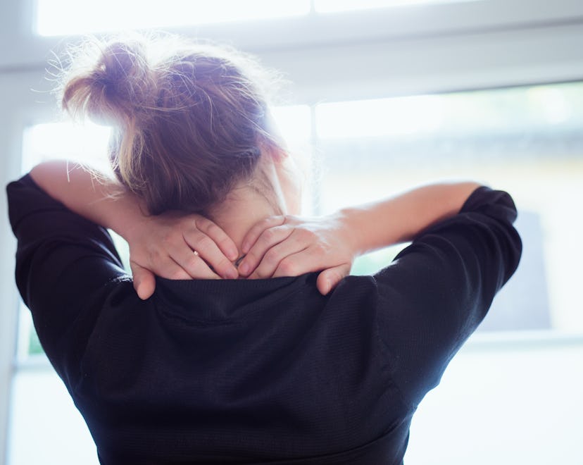 stressed woman rubbing her shoulders while looking out the window