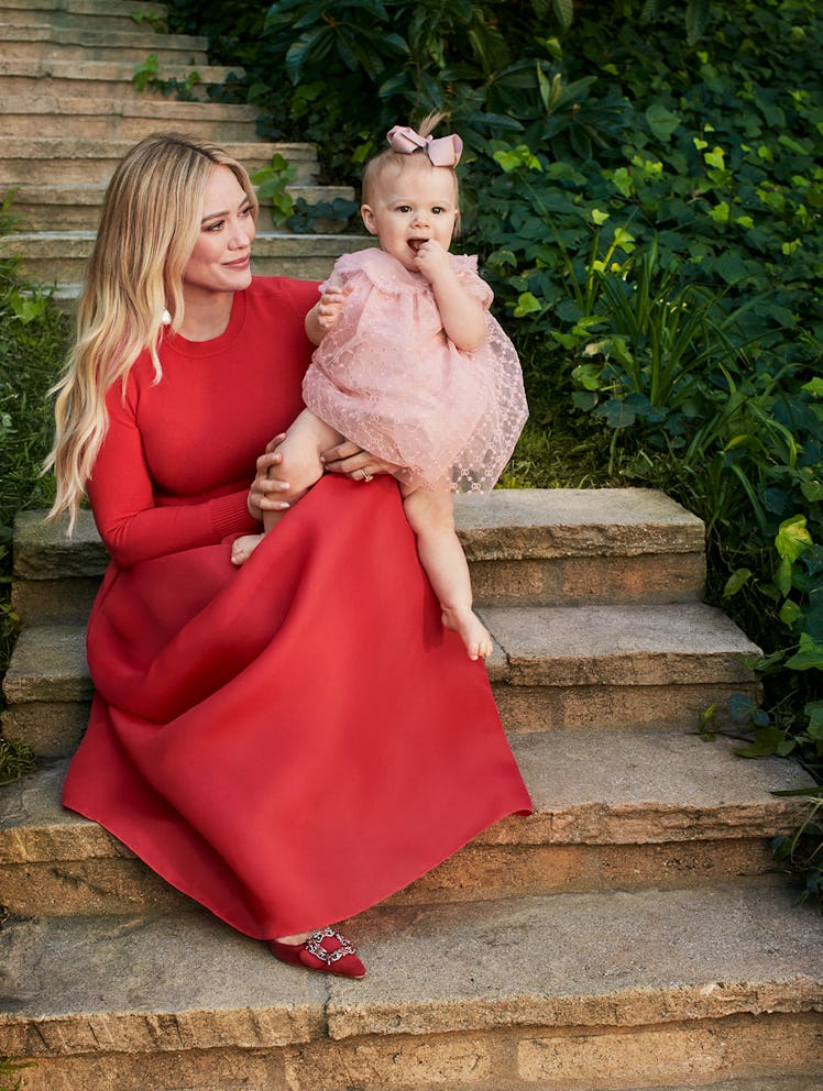 Hilary Duff wearing a red skirt and top, posing with her daughter on her lap.