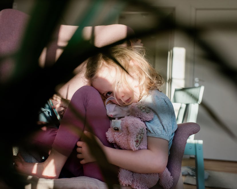 young girl curled up on a chair looking tired holding her toy at home