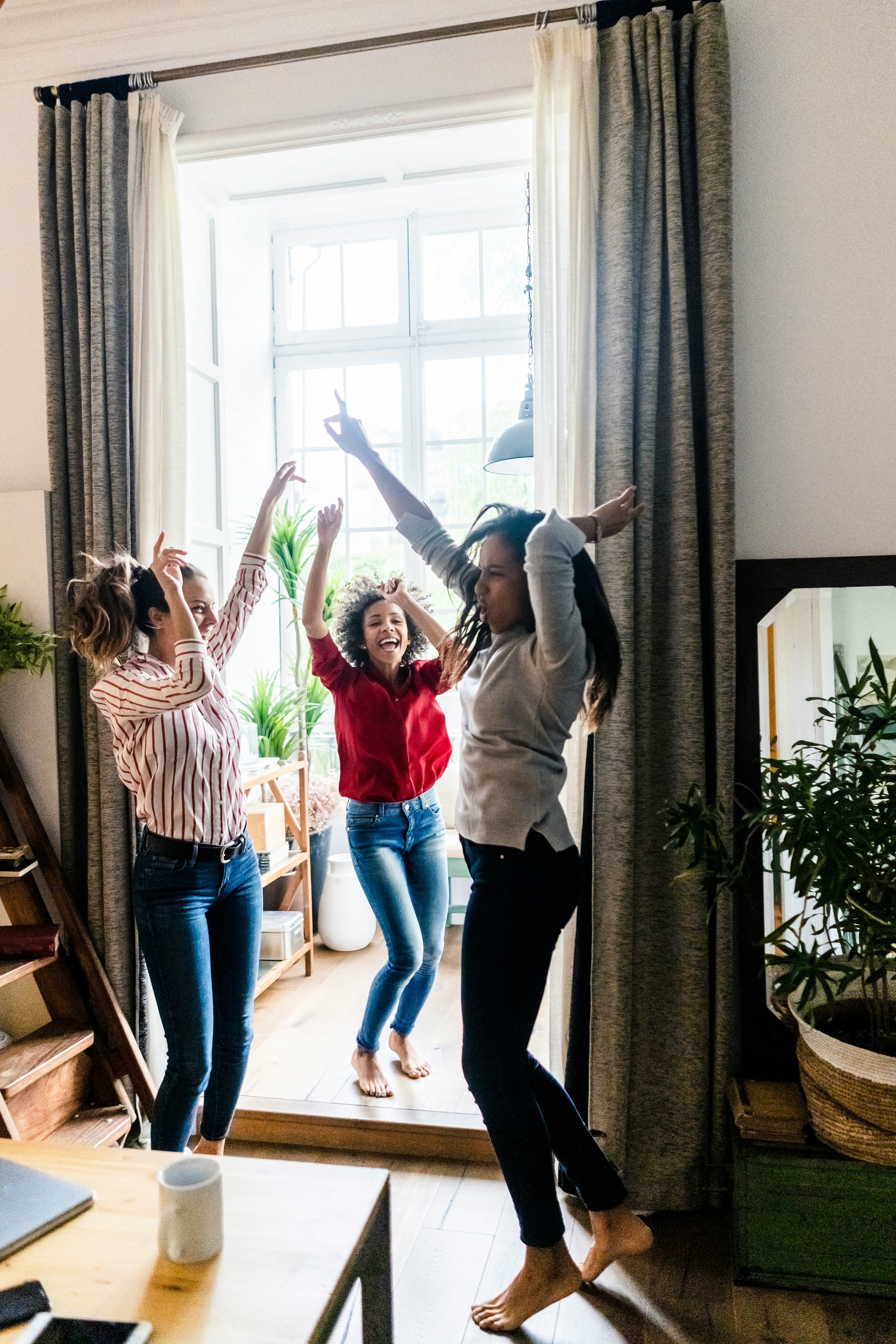 Three young women jumping up and down at home as their zodiac signs celebrate Galentine's Day 2022.