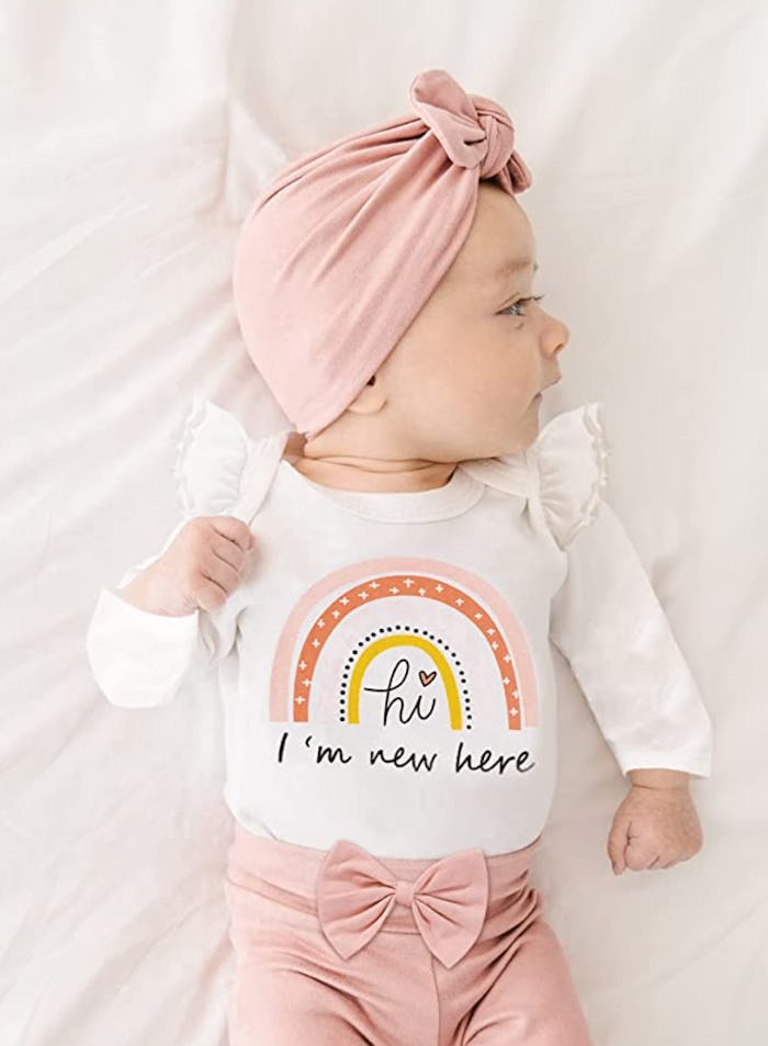 Baby laying down wearing pink hat, pink pants, and a rainbow onesie