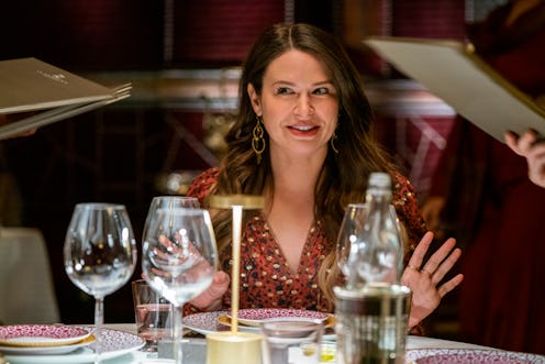 Katie Lowes as Rachel in Netflix's 'Inventing Anna.' She is wearing a red patterned dress and sittin...