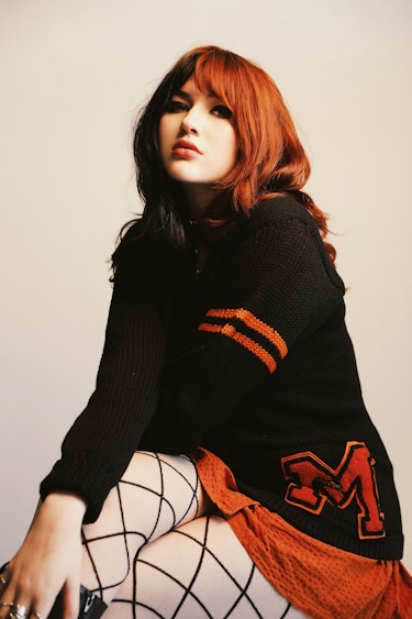 GAYLE poses in mesh tights, an orange mini skirt and a college sweater.