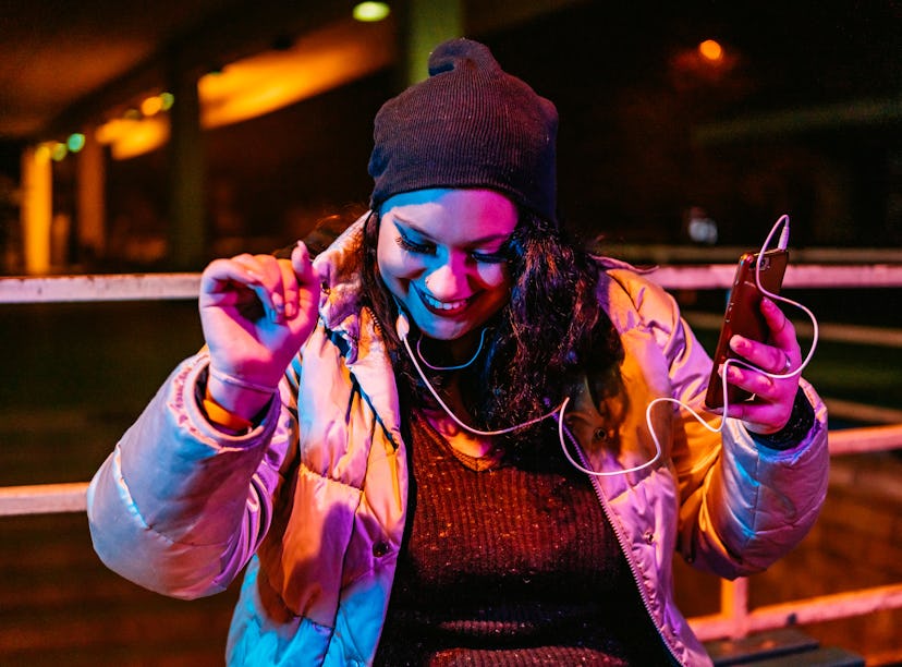Young woman listening to music on her phone, having the best week of February 14, 2022, per her luck...