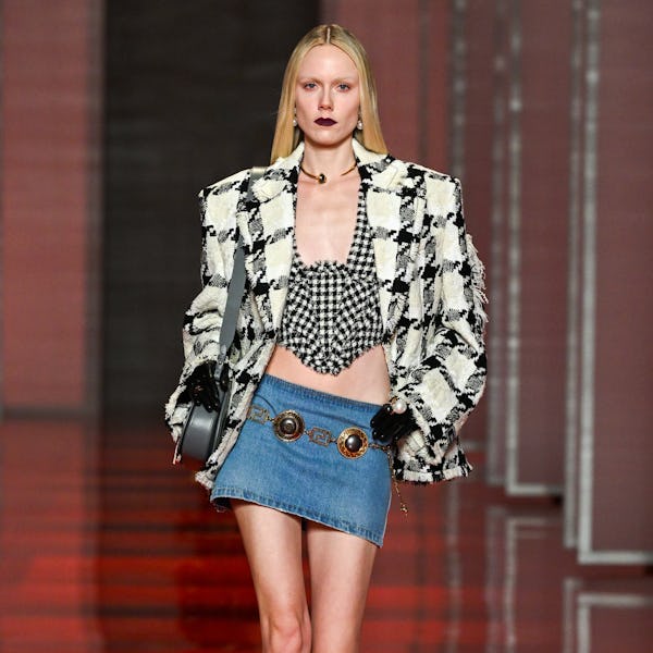 A model wearing a micro mini denim skirt and black and white blazer on the Versace runway