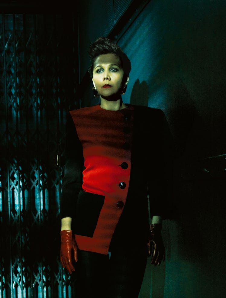 Maggie Gyllenhaal in a red-black jacket and red gloves in a dark room