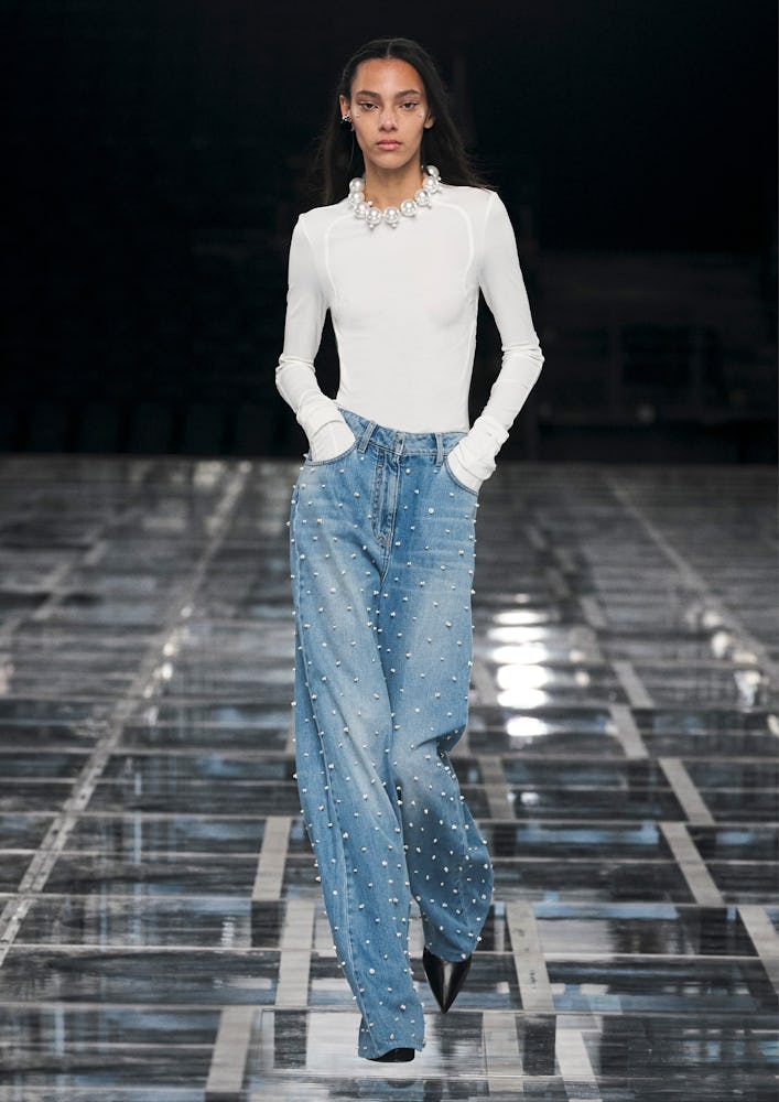 A model wearing a white bodysuit and baggy jeans with pearls on the Givenchy runway