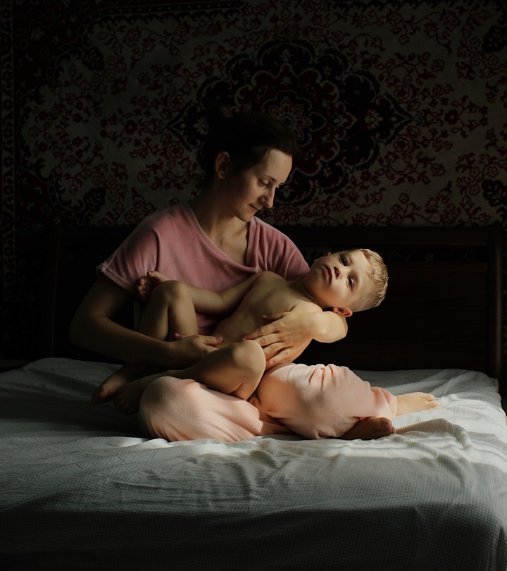 A mother cradles her toddler on a bed