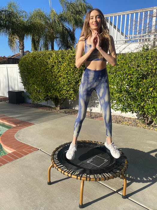 A brunette woman during the Ness trampoline workout in navy-beige tie-dye leggings and sports bra st...