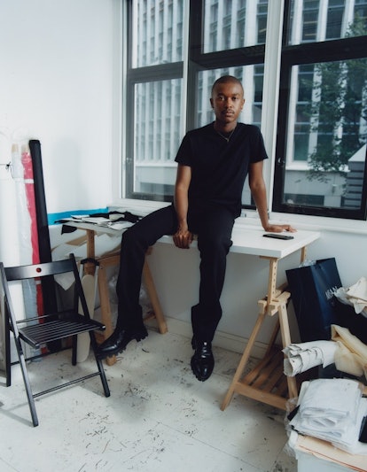 The designer Maximilian Davis sitting on a table in his London studio