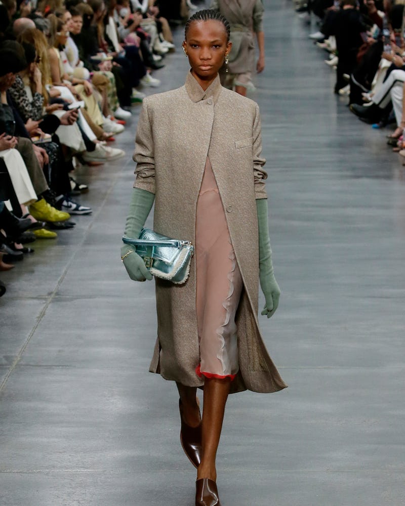 a model wearing a beige tailored coat and sheer dress on the Fendi runway