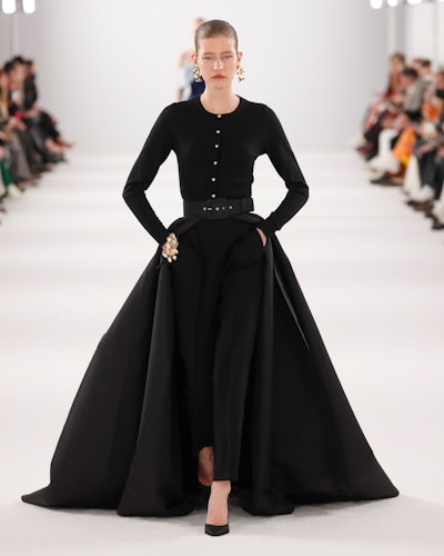 a model wearing a black top and pants with a train on the Carolina Herrera runway