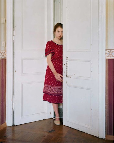 A person wearing a red dress hiding behind a door photographed by Alec Soth