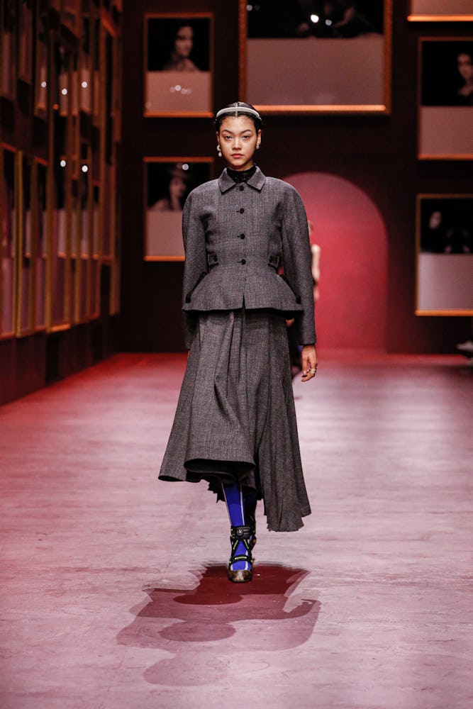 a model wearing a grey peplum blazer and asymmetric pleated maxi skirt on the Dior runway