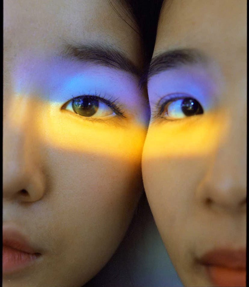 A close-up of a mirrored image of a woman with a blue and yellow light over her face in support to U...