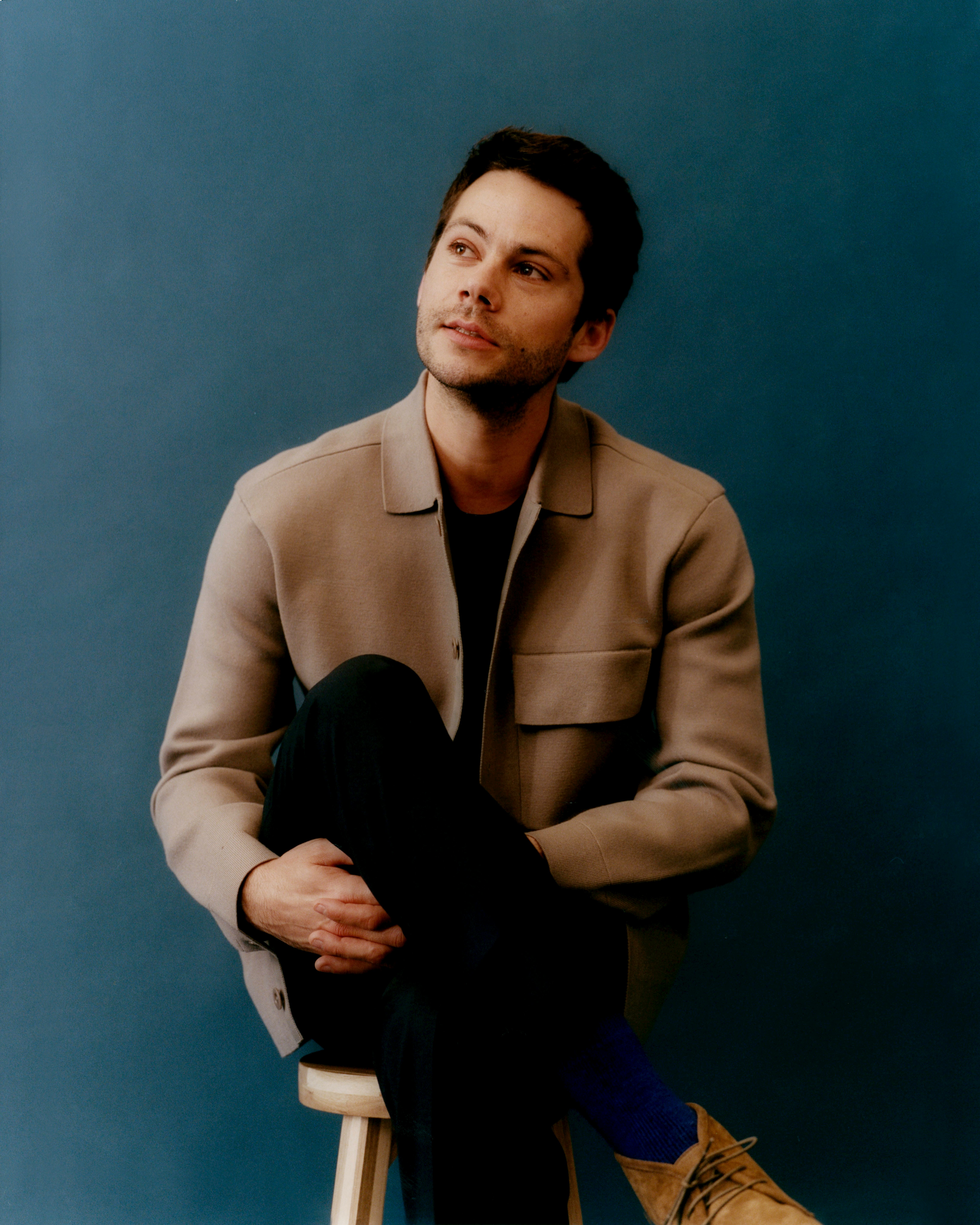 Dylan O&rsquo;Brien sitting legs-crossed and looking to his right