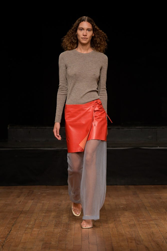 a model wearing an orange leather miniskirt over sheer pants on the Rejina Pyo runway