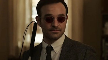 Charlie Cox wearing a grey suit, glasses, and blind stick as Matt Murdock