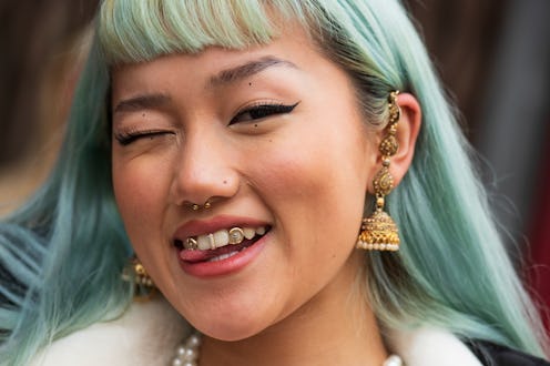 A person with blue hair smiles into the camera; they have a stud nose ring, similar to some of the b...