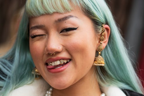 A person with blue hair smiles into the camera; they have a stud nose ring, similar to some of the b...