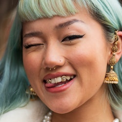 A person with blue hair smiles into the camera; they have a stud nose ring, similar to some of the b...