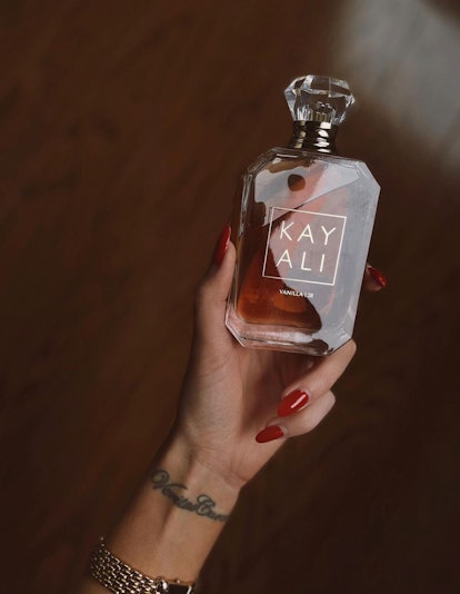 red-manicured hand holding a bottle of Kayali Vanilla 28