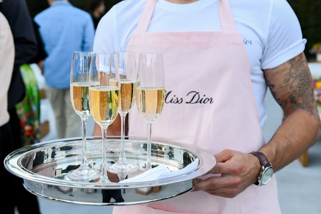 Glasses of Moët Chandon passed around by a male server in a pink apron with "Miss Dior" written on i...