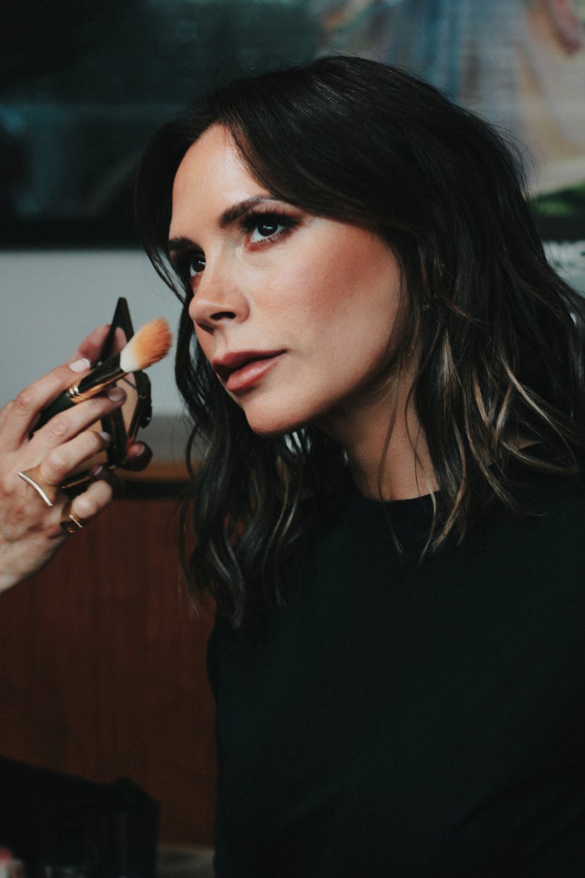 A closeup of Victoria Beckham looking away as someone is doing her makeup 