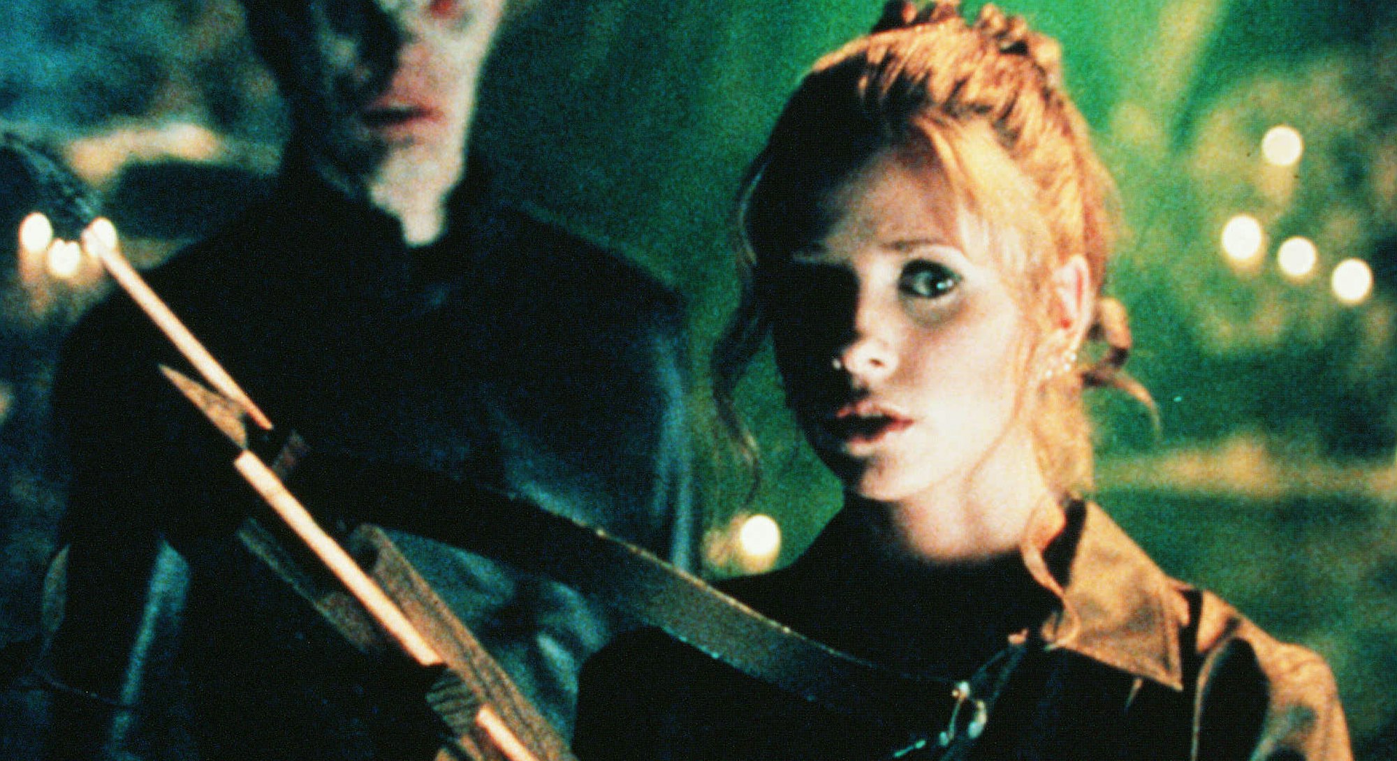 Sarah Michelle Gellar as Buffy The Vampire Slayer holding a crossbow in a scene and a vampire behind...
