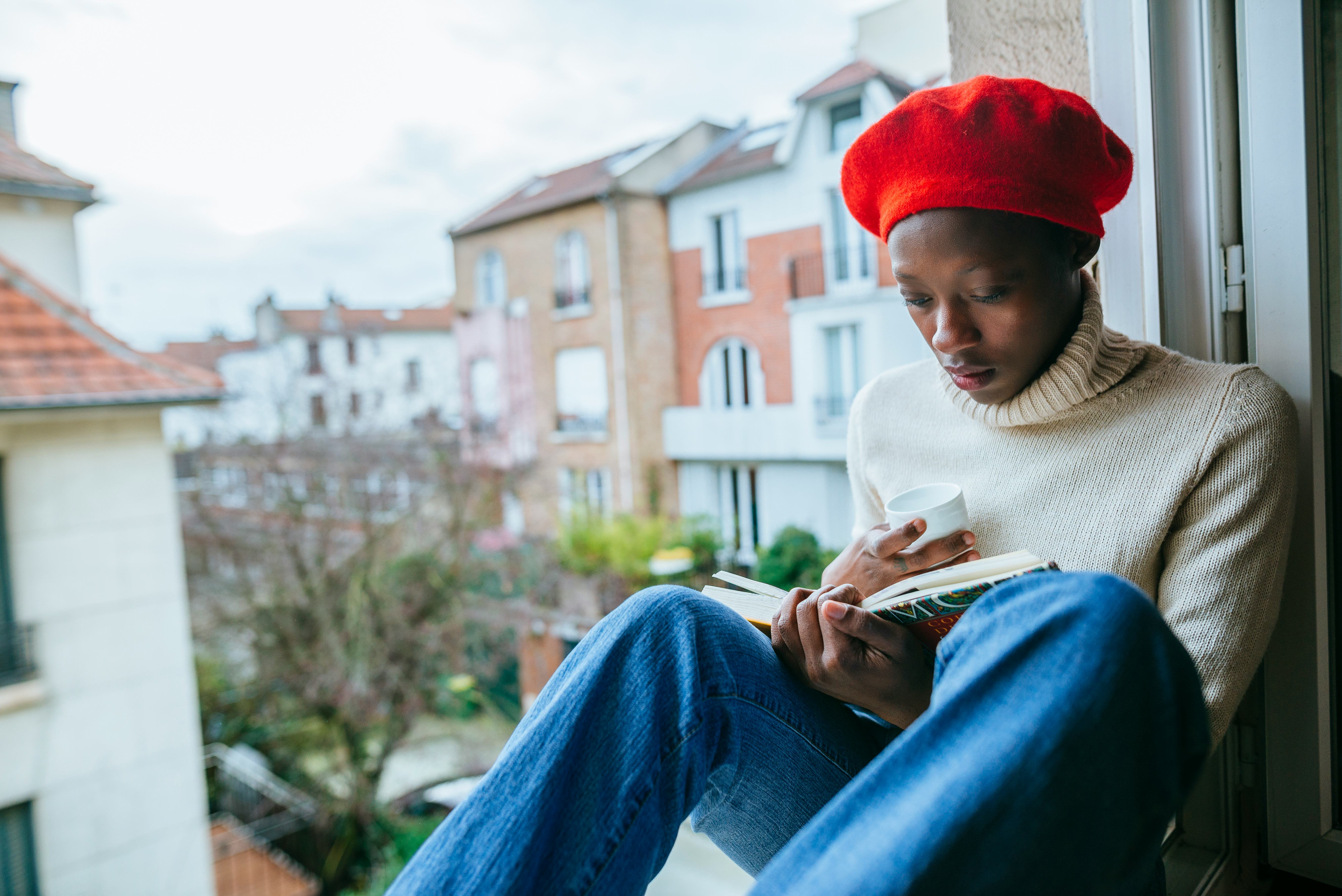 Woman sitting in a window with a book and a cup.