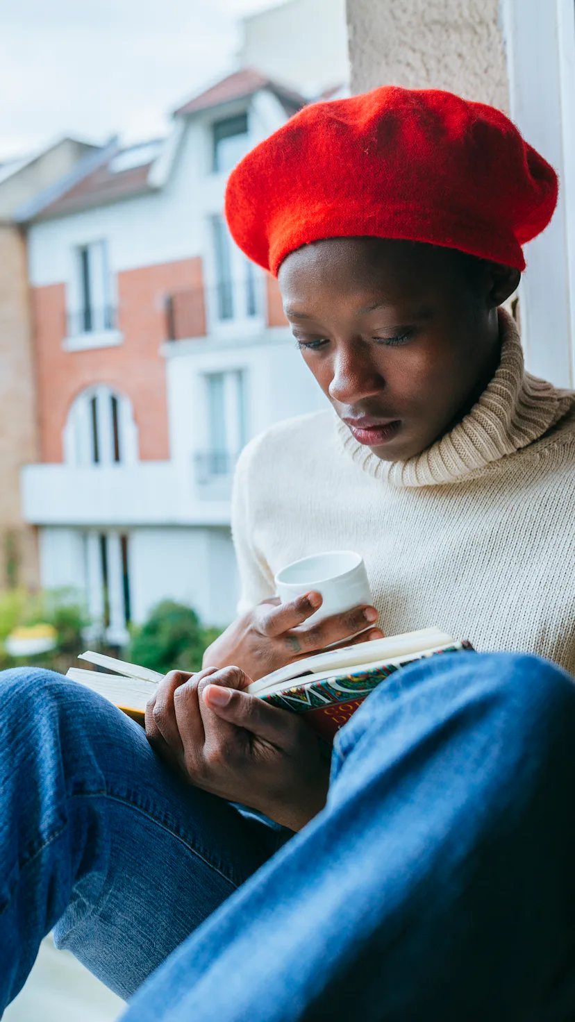 Woman sitting in a window with a book and a cup.