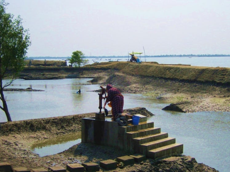 a woman pumps fresh deep. groundwater in coastal Bangladesh while surrounded by brackish surface wat...