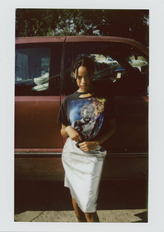 Kilo Kish posing in a black graphic shirt and a white skirt