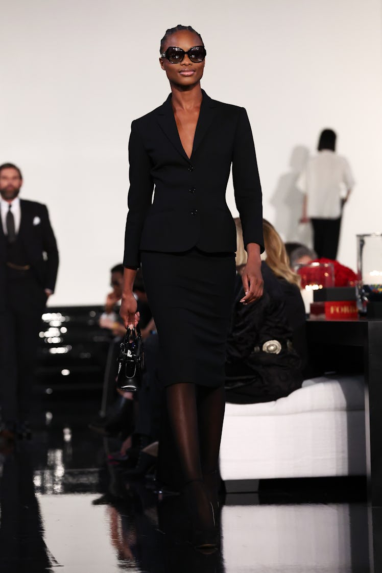 Model on the NY Fashion Week Fall 2022 runway in a Ralph Lauren black skirt and blazer, carrying a b...